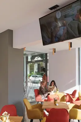 two women sitting in a restaurant with a flat screen tv at Meni Hotel & Apartments UNDER NEW MANAGEMENT in Athens
