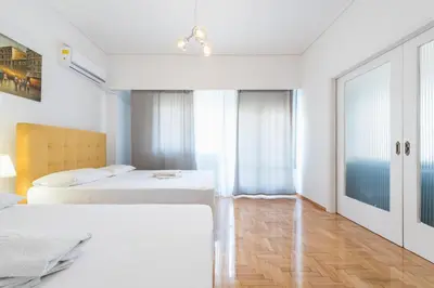 a white bedroom with two beds and a window at Victoria Diamond Suites Apartments in Athens