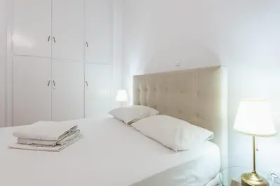 a white bedroom with a bed and a lamp at Victoria Diamond Suites Apartments in Athens