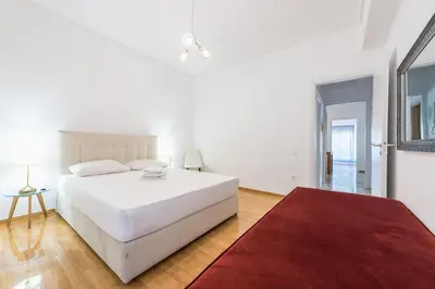 a white bedroom with a white bed and a red rug at Victoria Diamond Suites Apartments in Athens