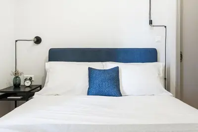 a white bed with a blue pillow on it at Deluxe & Stylish 2BD Apartment in Pangrati by UPSTREET in Athens