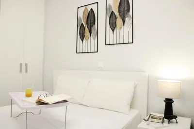 a white bedroom with a bed with a table and a lamp at ARIS Piraeus Marina in Piraeus