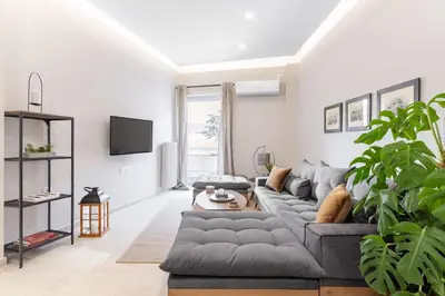 a living room with a gray couch and a tv at Deluxe 3-BDRM Urban-industrial Apt at Acropolis in Athens