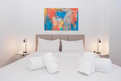 a white bed with white pillows and a painting at Melodies of Athens apt in Ilisia neighbourhood in Athens