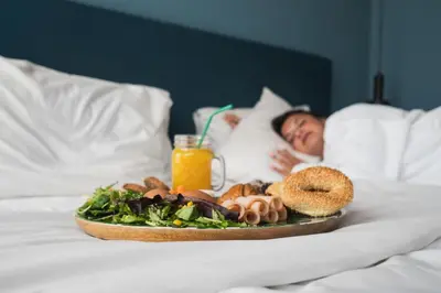 a person laying in bed with a plate of food at COLORS Hotel Athens in Athens
