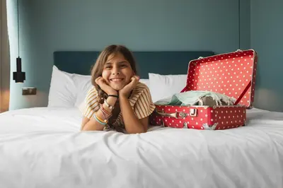 a little girl laying on a bed with a suitcase at COLORS Hotel Athens in Athens