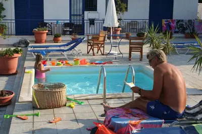 a man sitting on a towel in front of a swimming pool at Helios Hotel in Agia Marina Aegina