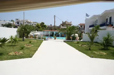 a walkway through a resort with palm trees and buildings at Helios Hotel in Agia Marina Aegina