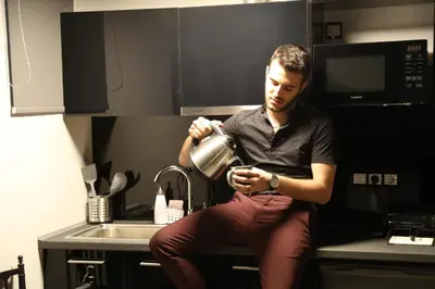 a man sitting on a kitchen counter drinking from a pot at Rooster Suites in Athens