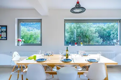 a dining room with a large wooden table and white chairs at Your Home2b in Paianía