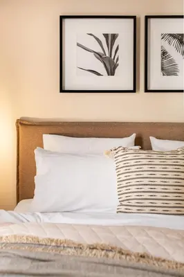 a bed with white pillows and framed pictures on the wall at Acropolis View 2-Bedroom Apt, Minimal-Safari Vibe, Big Balcony! in Athens
