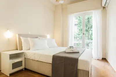a white bedroom with a bed and a window at La casa di Plaka in Athens