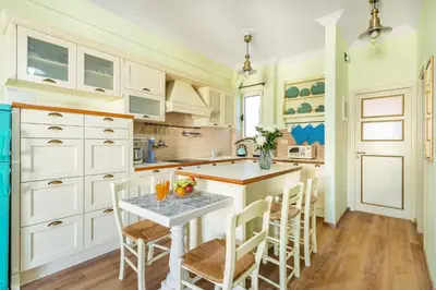 a kitchen with white cabinets and a table with chairs at Bright, Calming Retreat With a Balcony Near Metro! in Athens
