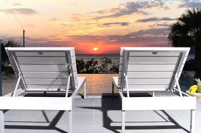 two chairs sitting on a deck watching the sunset at Black Diamond Luxury Beachfront Villa Selenia in Sounio