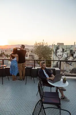 a man sitting at a table with a laptop on a balcony at Melo Athens in Athens