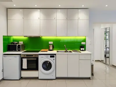 a kitchen with white cabinets and a green wall at KYMA Apartments Athens 18 in Athens