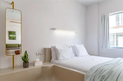 a white bedroom with a bed and a mirror at LOFUS Bio-Suites in Athens