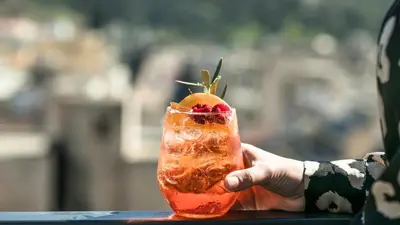 a hand holding a drink with a fruit on top at Play Theatrou Athens a member of Brown Hotels in Athens