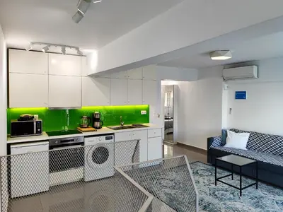 a kitchen with white cabinets and a green accent wall at KYMA Apartments Athens 19 in Athens