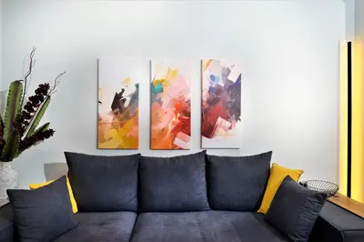 a couch in a living room with four paintings on the wall at Cozy Apt in Ilisia with Urban Forest View in Athens