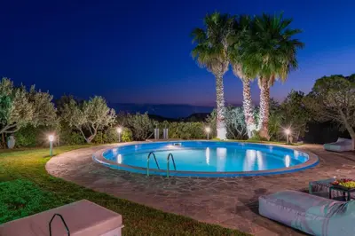 a swimming pool at night with palm trees at Cuervo Poolside Villa in Kalívia Thorikoú