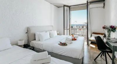 a hotel room with two beds and a desk and a window at Apollo Resort in Agia Marina Aegina