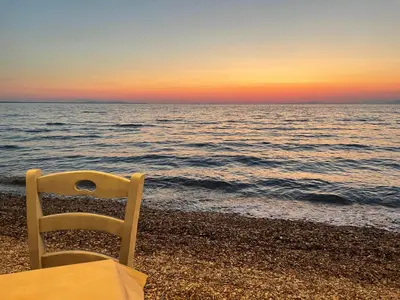 a chair sitting on the beach at sunset at blue cielo sunny apartment in Palaiá Fókaia