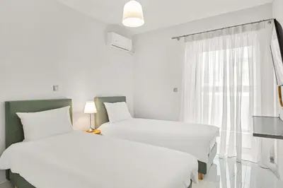 a white bedroom with two beds and a window at BillyMare central Glyfada apartment in Athens