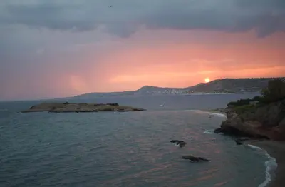 a sunset over the ocean with a island in the water at Studio Agia Marina Koropi in Aghia Marina