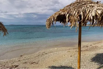 a straw umbrella on a beach with the ocean at Seaside Villa Lagonisi in Kalívia Thorikoú