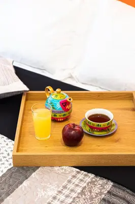 a tray with a cup of orange juice and an apple on a bed at Calypso Apartment in Athens