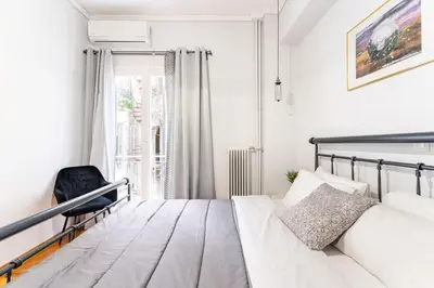 a white bedroom with a bed and a chair at Downtown Cute Apt in the Heart of Plaka (+Netflix) in Athens
