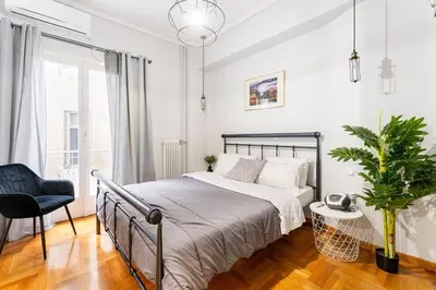 a white bedroom with a bed and a chair at Downtown Cute Apt in the Heart of Plaka (+Netflix) in Athens
