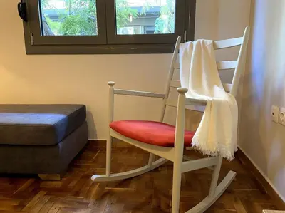 a wooden rocking chair with a red cushion and a window at Cozy and comfortable apartment in Athens Center in Athens
