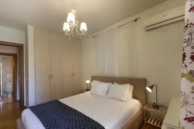 a bedroom with a bed with white sheets and a chandelier at 3BR Prime APT a breath away from the Acropolis! in Athens