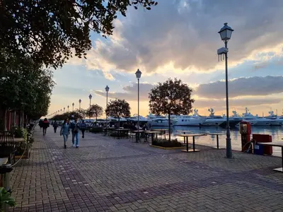 a group of people walking down a sidewalk near the water at Arman Group in Athens