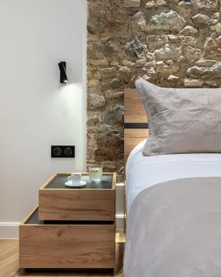 a bed with a wooden night stand next to a stone wall at J&A Luxury Residence in Athens