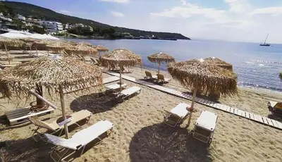 a beach with straw umbrellas and lounge chairs and the ocean at Παραθαλασσιο στουντιο Μιχαλιας Sea view studio Michalias Νουμερο 8 in Agia Marina Aegina
