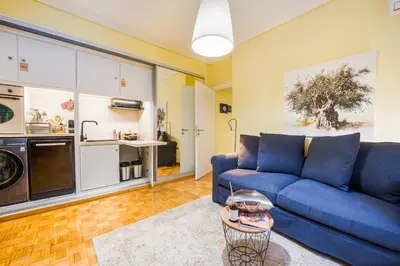 a living room with a blue couch and a kitchen at Magnificent Bnb Athens Voula in Athens