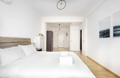 a white bedroom with a large bed and a clock on the wall at Lovely apartment in the heart of Athens in Athens