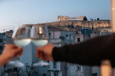 a person holding two glasses of white wine at Acropoli's balcony in Athens