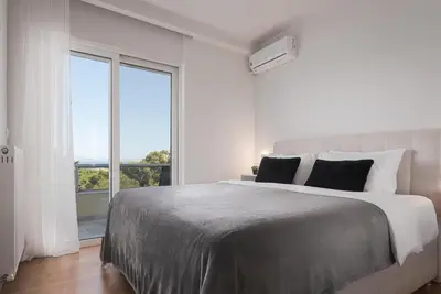 a white bedroom with a large bed and a large window at Athenian Riviera Sea View Penthouse in Vari