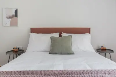 a bed with white sheets and pillows and two tables at Stellar 3BR Apartment with Balcony by UPSTREET in Athens
