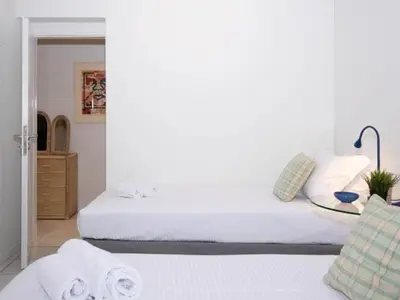 a white bedroom with two beds and a table at Vouliagmeni‘s Secret Garden near the Sea in Athens