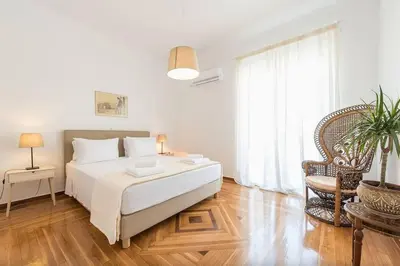 a white bedroom with a bed and a chair at Casa Pamisou near Attiki metro station in Athens