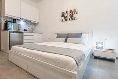 a white bedroom with a large bed and a kitchen at Phaedrus Living: City Center Executive Flat Stadiou in Athens