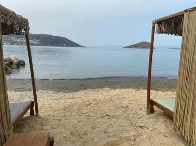 a beach with two benches on the sand and the water at Architect's summer house by the beach in Porto Rafti