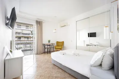 a white bedroom with a large bed and a living room at Cozy Studio by the sea in Paleo Faliro in Athens