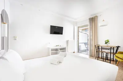 a white living room with a tv and a table at Cozy Studio by the sea in Paleo Faliro in Athens