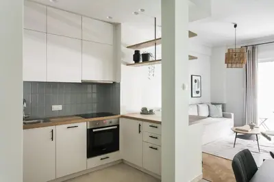 a kitchen with white cabinets and a living room at Dazzling 1BR Apartment in Koukaki by UPSTREET in Athens